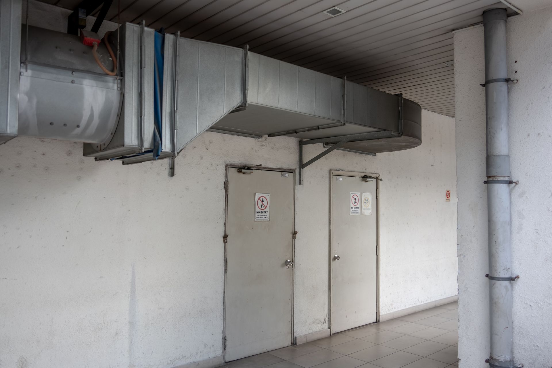 Hallway with two doors. Ventilation ductwork overhead, and a vertical pipe on the right.