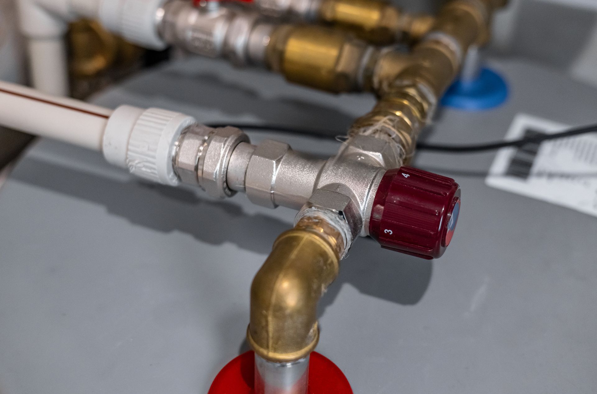 Plumbing with a red valve. Brass and white pipes connect, and a dark red knob regulates water flow.