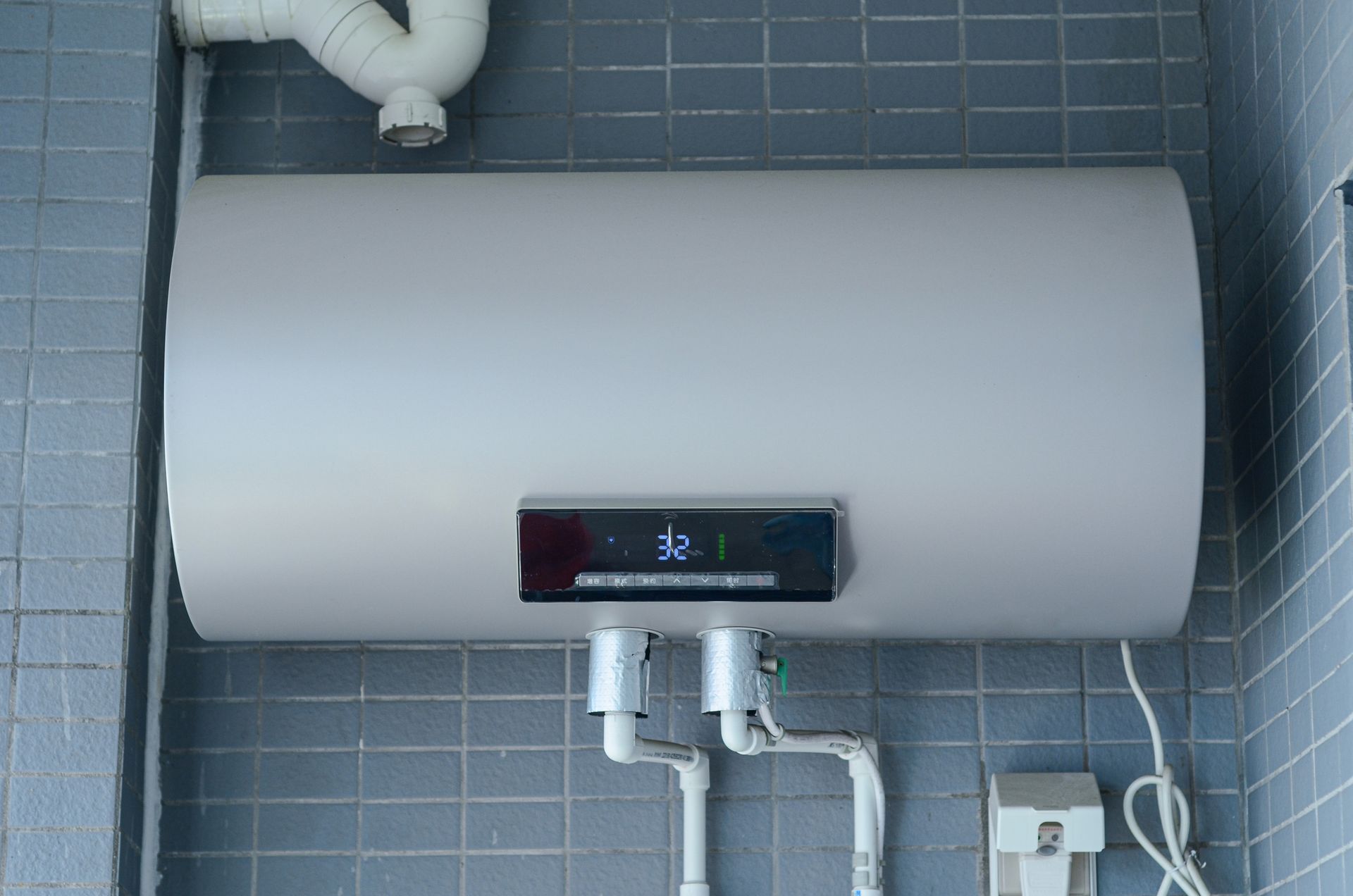 White water heater with digital display on a tiled wall; temperature reads 32.