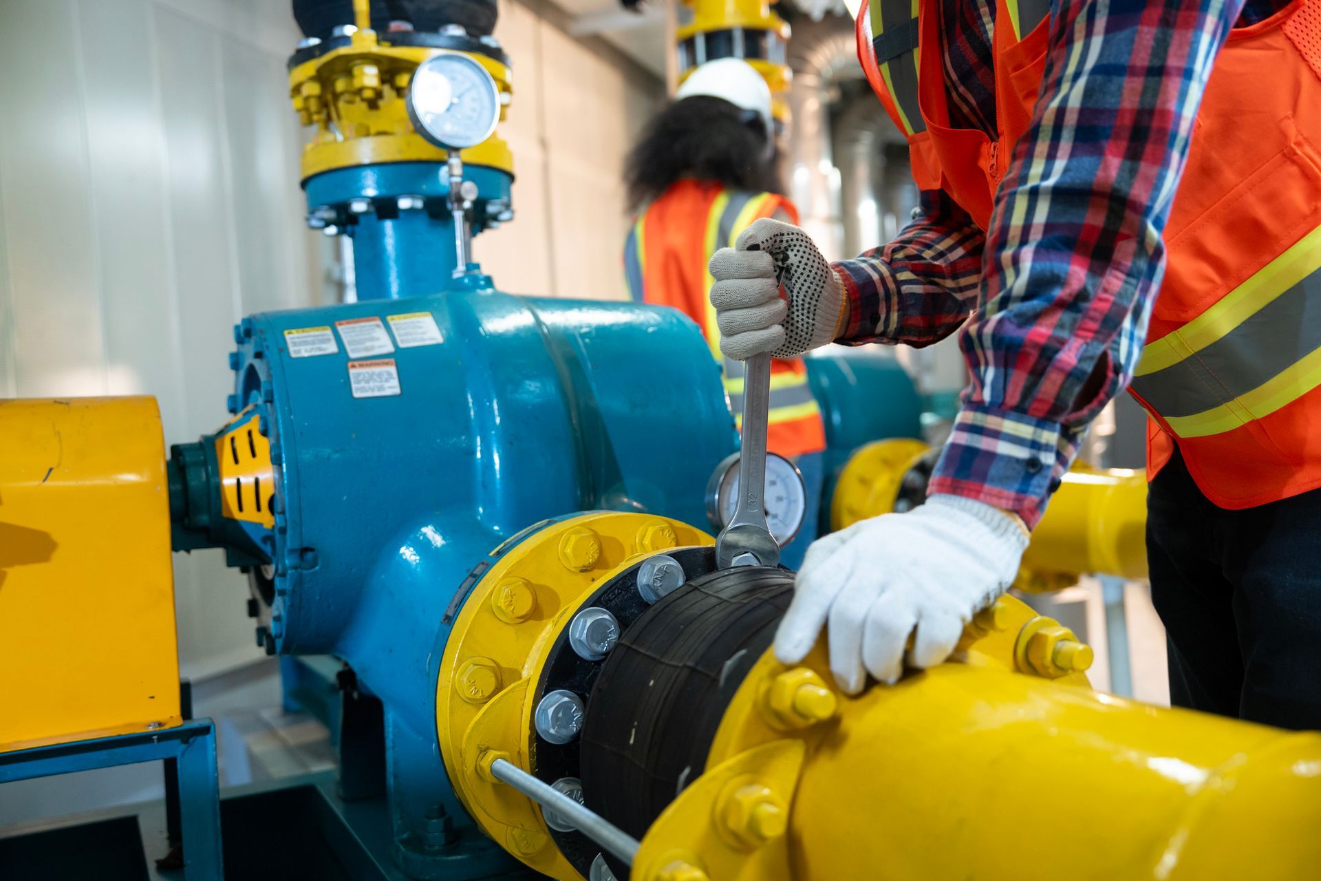Worker in safety gear using a wrench on industrial machinery, indoors.