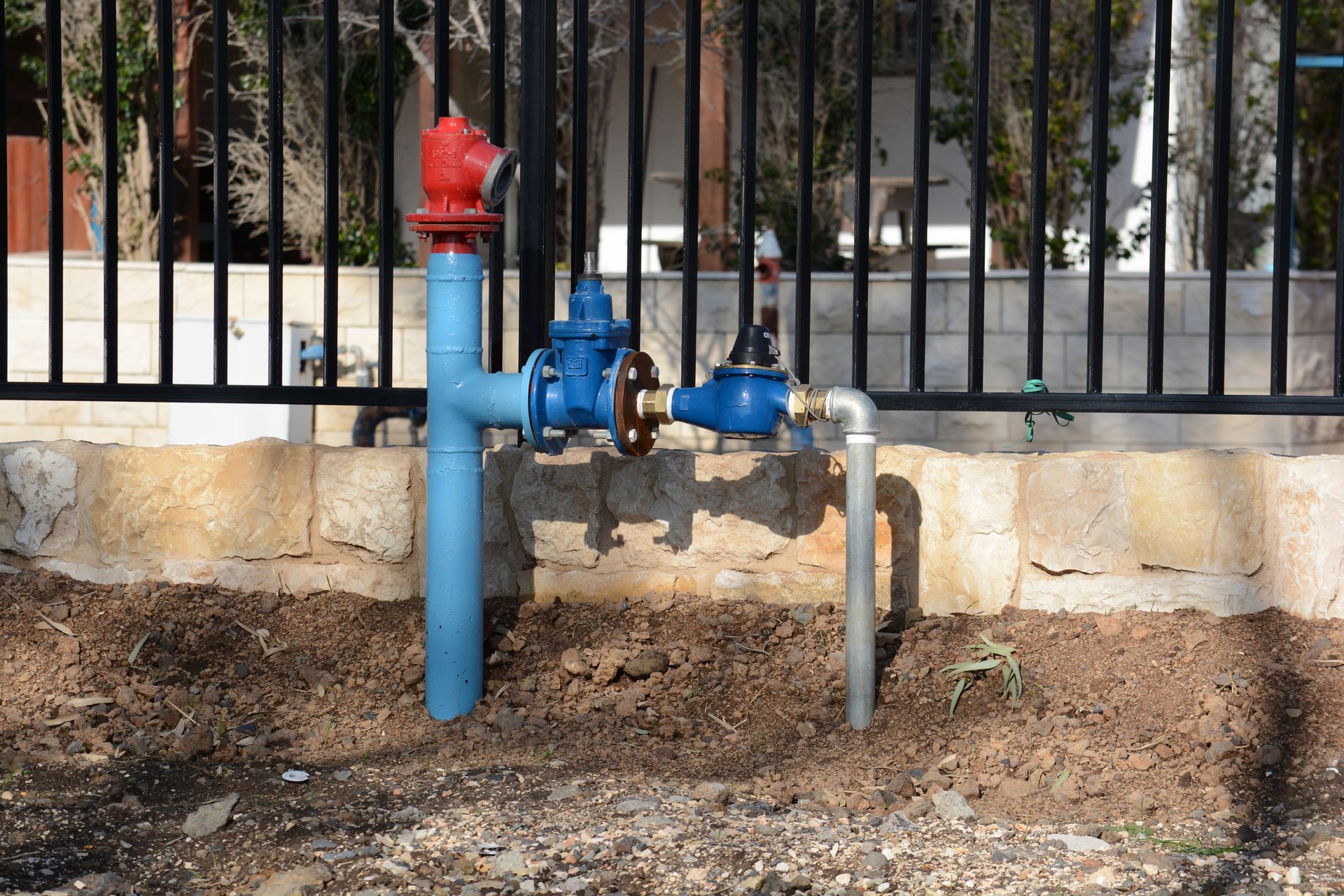 Blue and red water pipes and a hydrant, set against a fence and earth.
