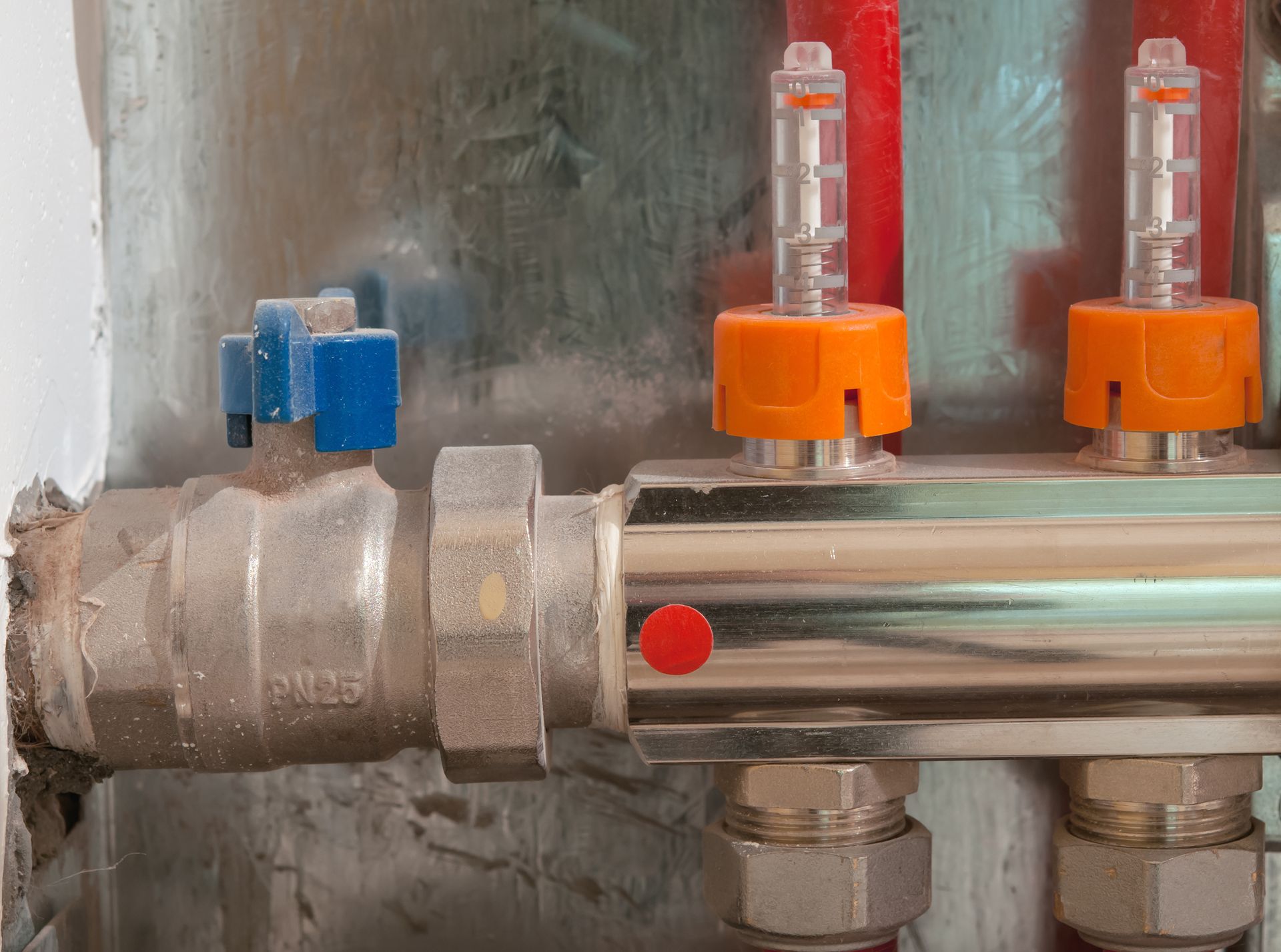 Close-up of silver pipes with red and blue valves and orange flow meters, mounted on a wall.