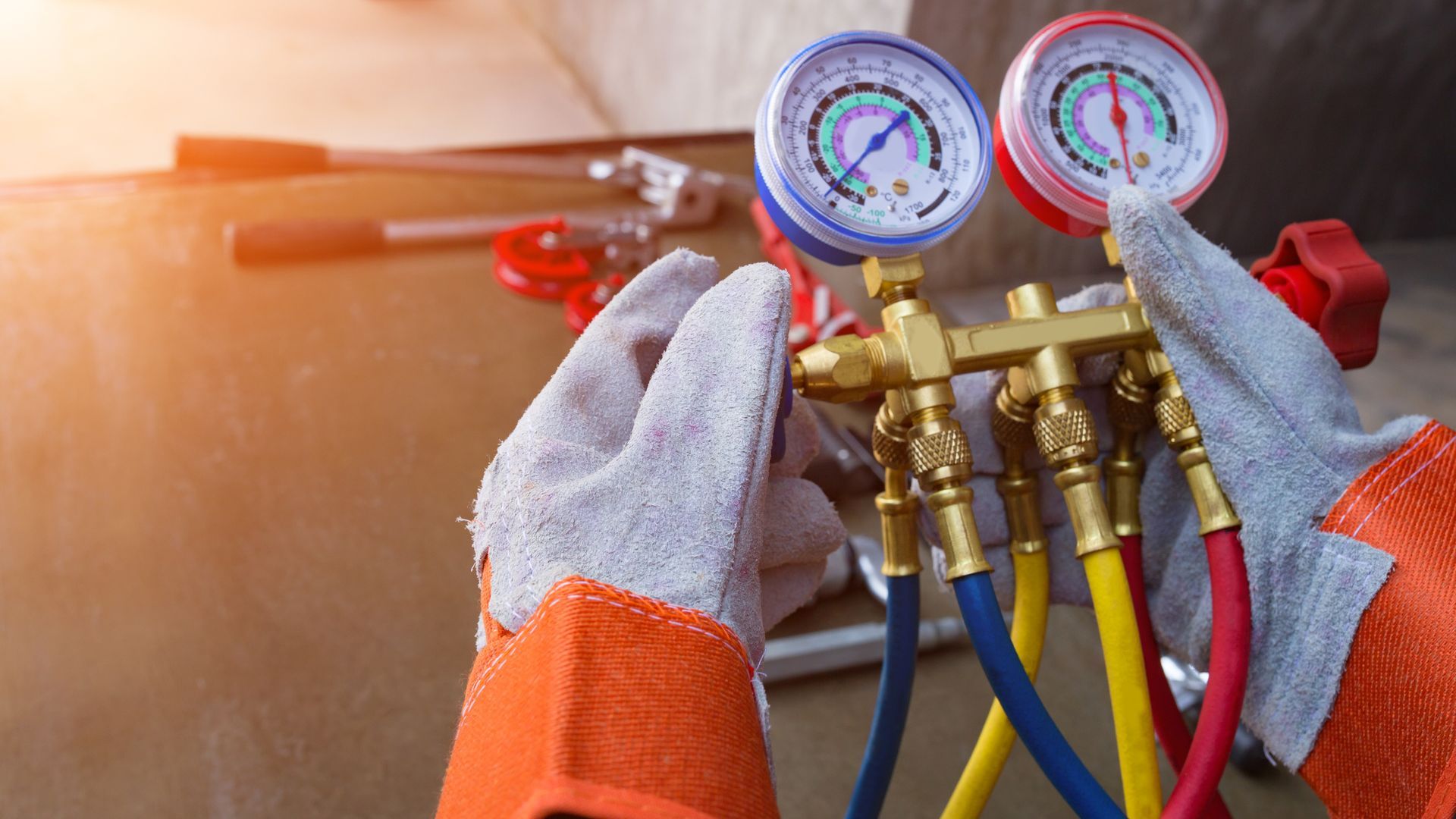 A person wearing gloves is using gauges connected to hoses to work on an HVAC system.