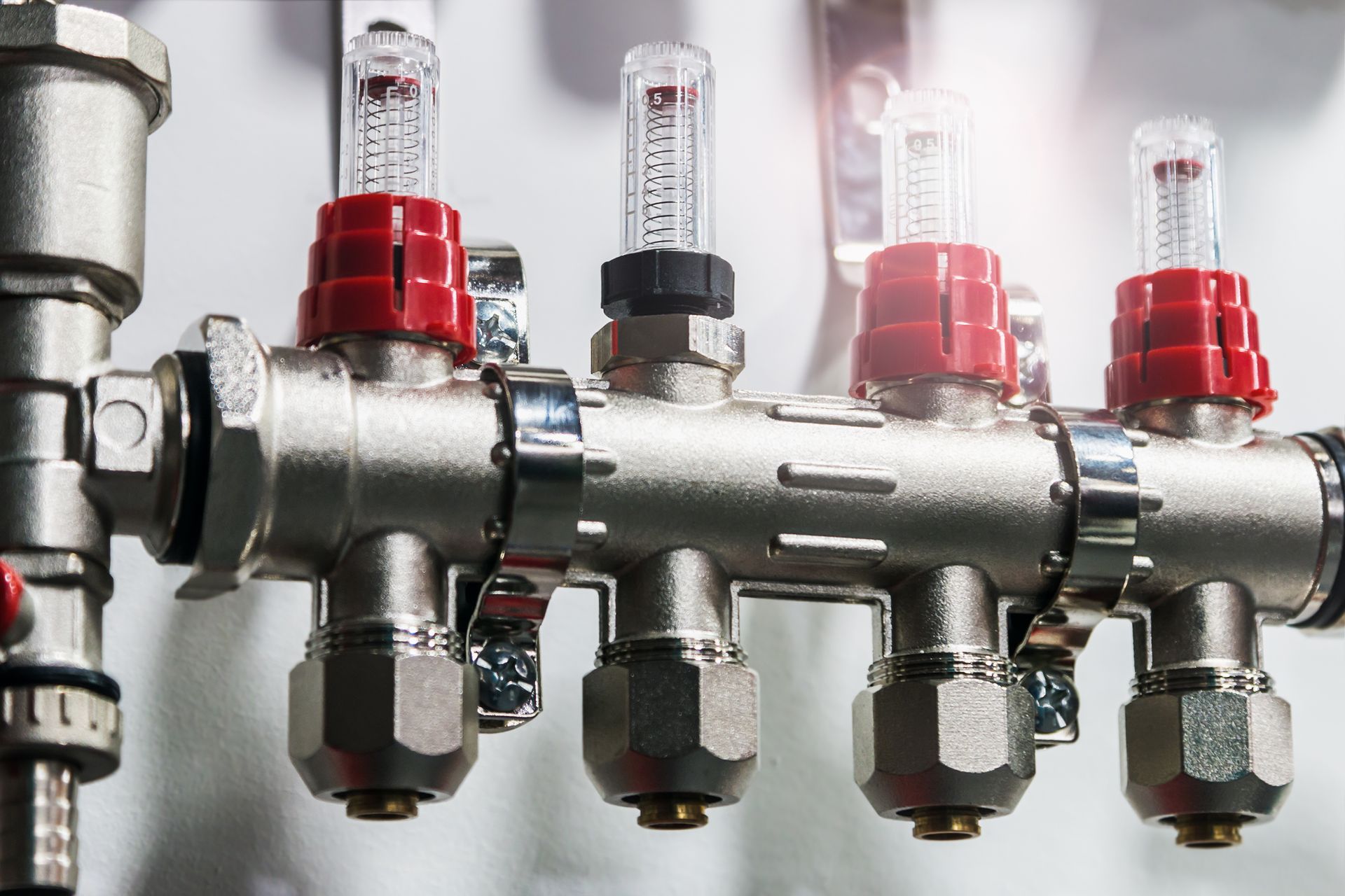Metal plumbing manifold with red and black valves, and clear flow meters.