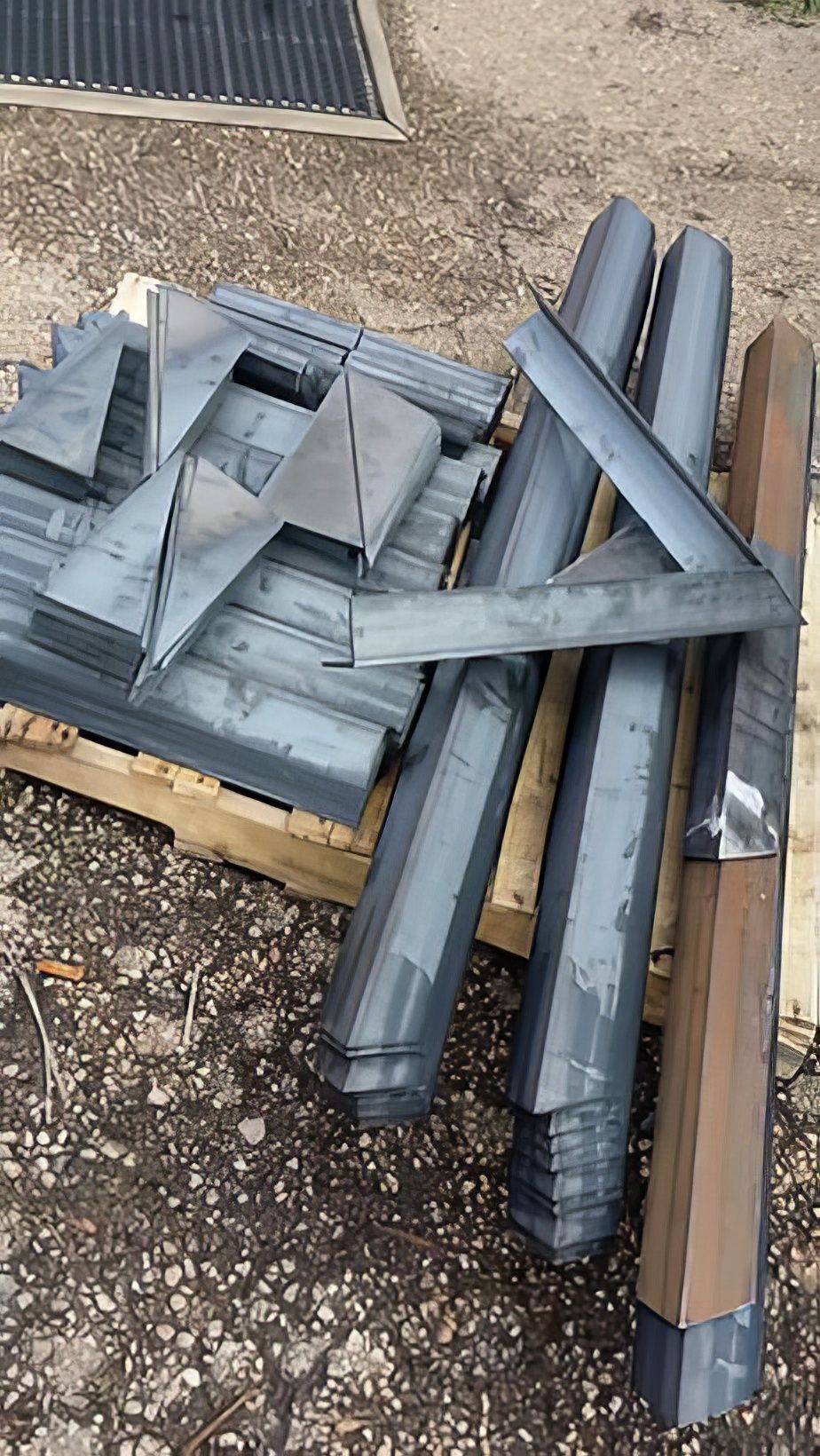 Pile of gray metal ductwork and pipes stacked on a wooden pallet outdoors.