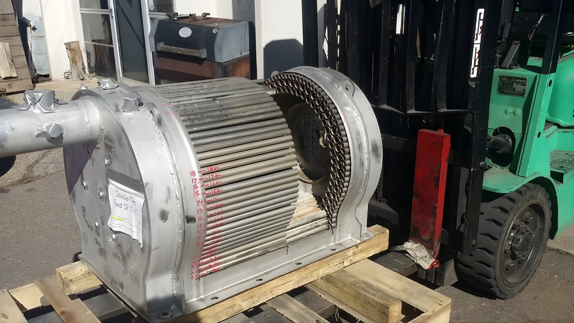 Industrial motor or blower housing on a pallet beside a green forklift in a warehouse.