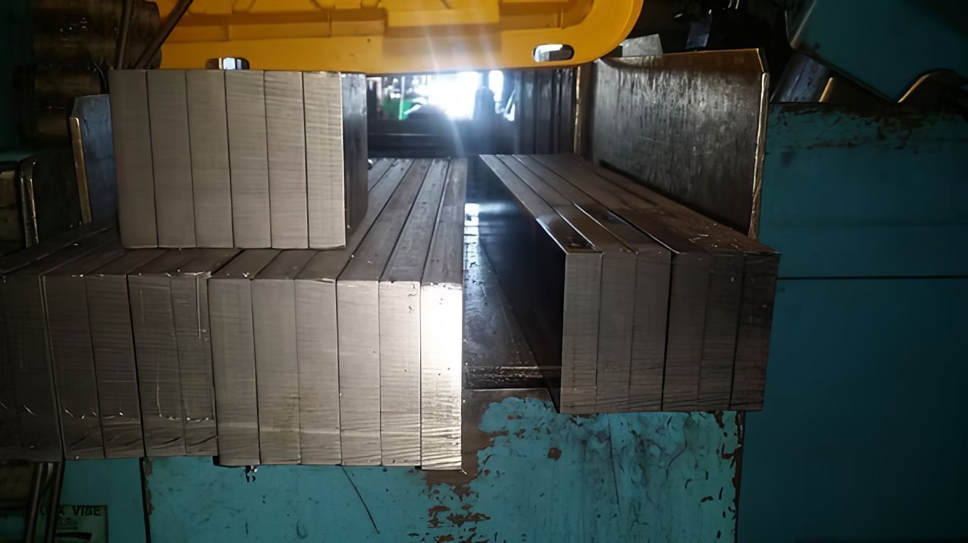 Stacked metal sheets loaded in a factory hopper under an overhead crane