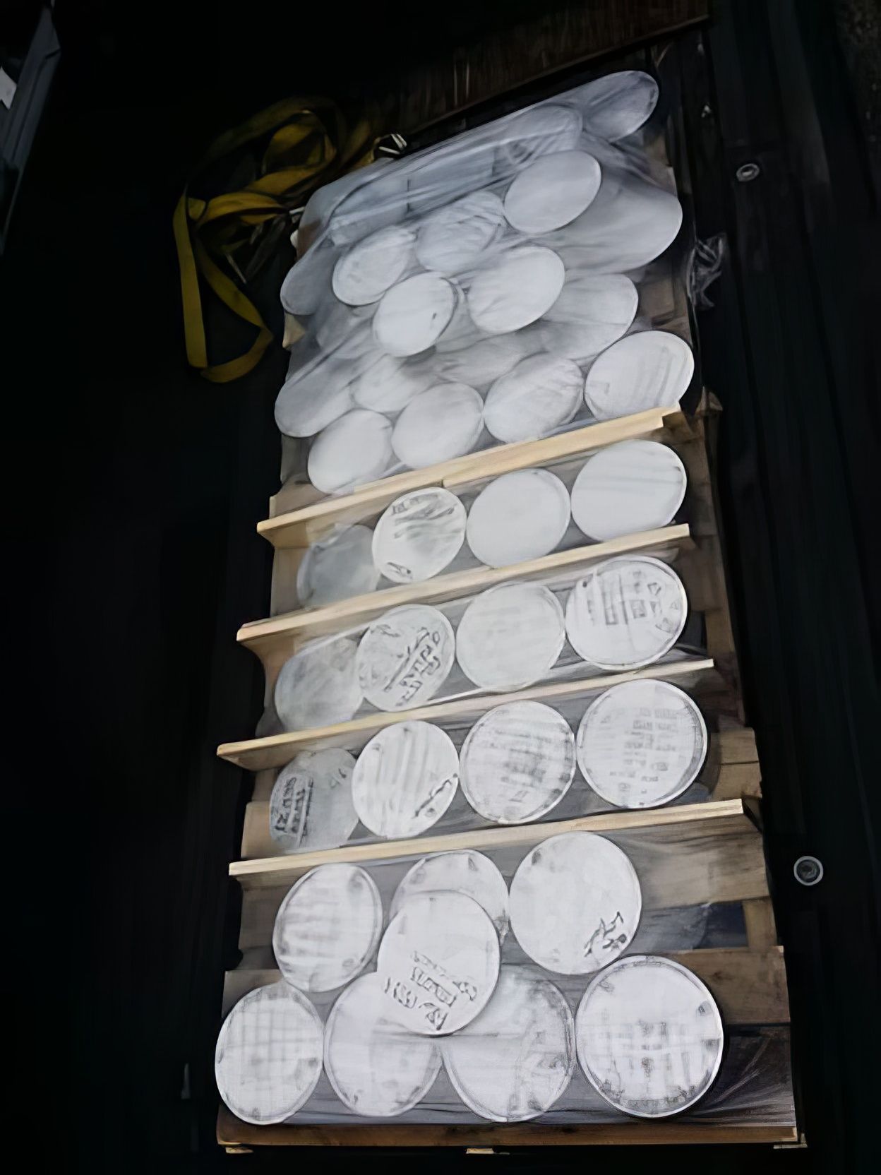 Stacked white cylindrical rolls secured with wooden slats inside a dark vehicle or cargo space