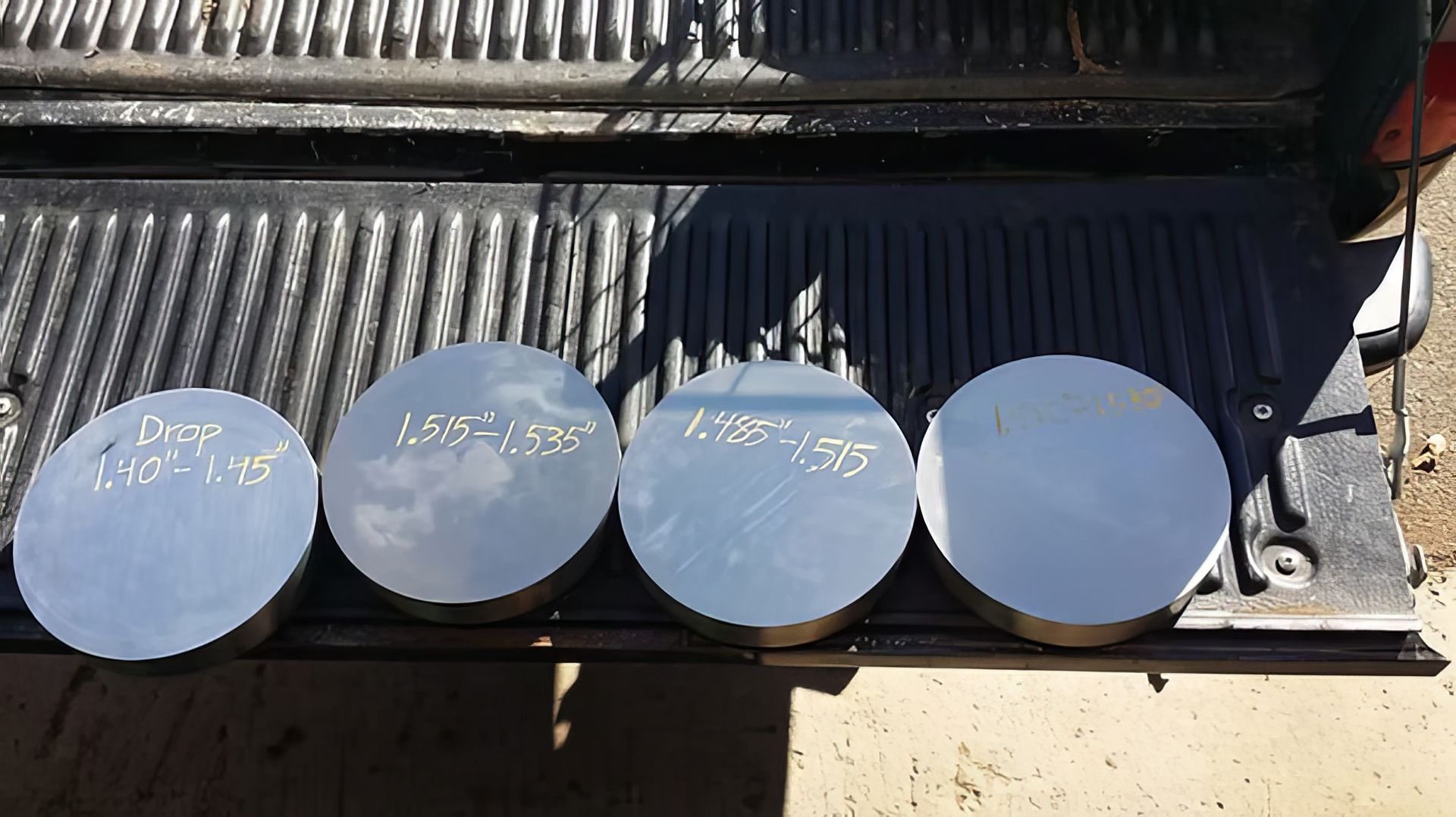 Four round metal lids lined up on a ribbed black grill in bright sunlight.