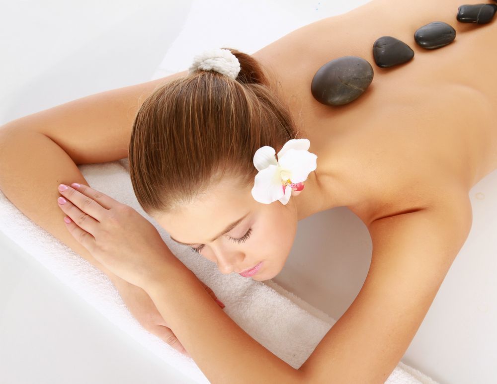 A Woman is Laying on a Table With Rocks on Her Back — Kerry's Body Therapy in Millner, NT