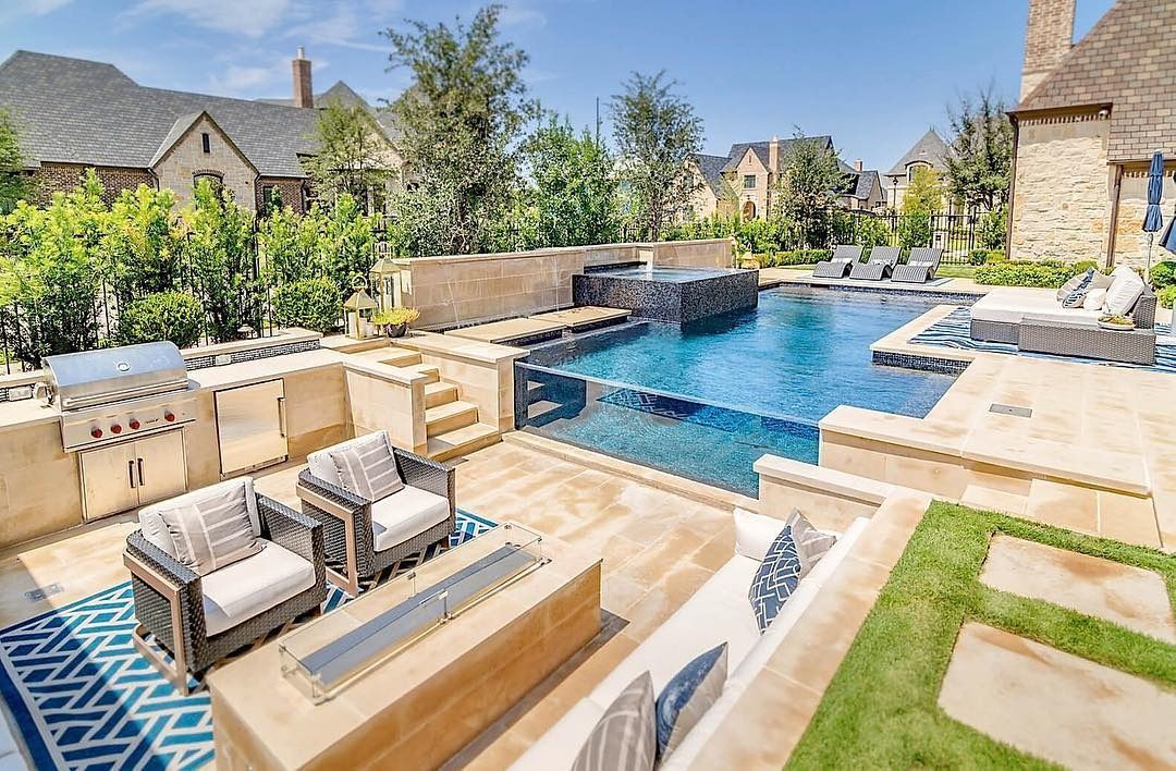 Luxury backyard pool with stone seating, loungers, and landscaped patio under a sunny sky