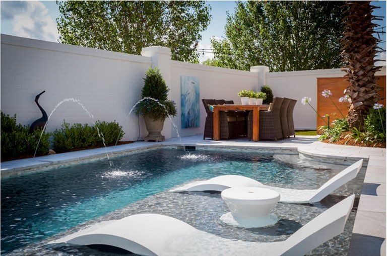 Modern backyard pool with waterfall spa, lounge chairs, patio dining set, and palm trees