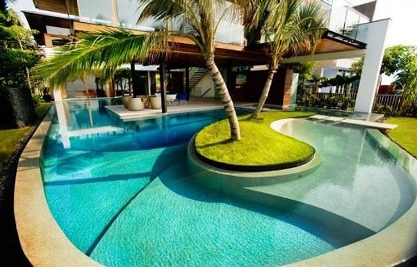 Curved turquoise resort pool with palm trees and a small grassy island