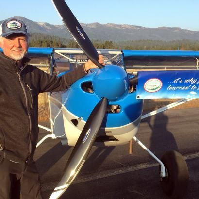 A man stands in front of a blue plane that says it 's why i learned to fly