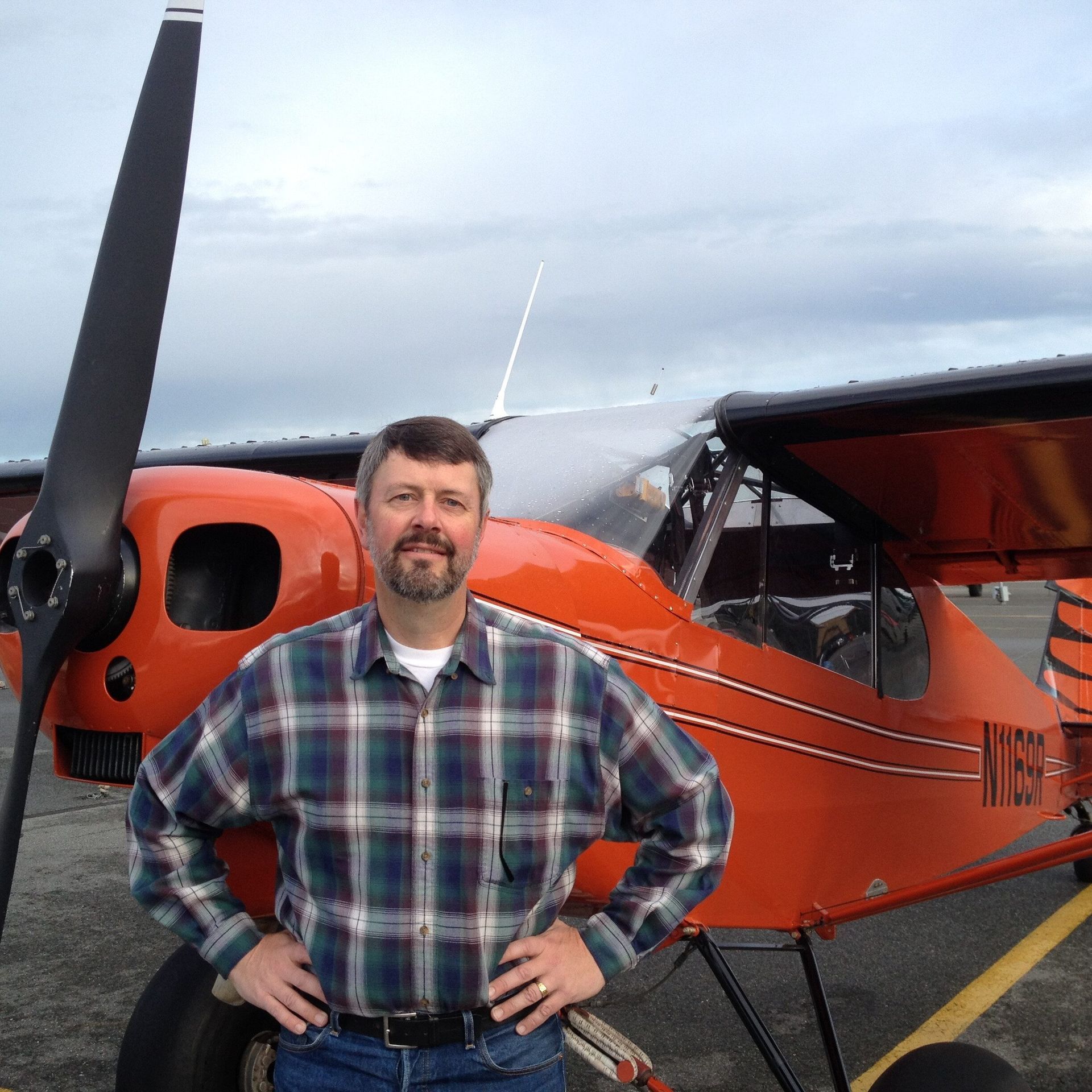 A man in a plaid shirt stands in front of an orange airplane