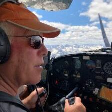 A man wearing headphones and sunglasses is sitting in the cockpit of an airplane.