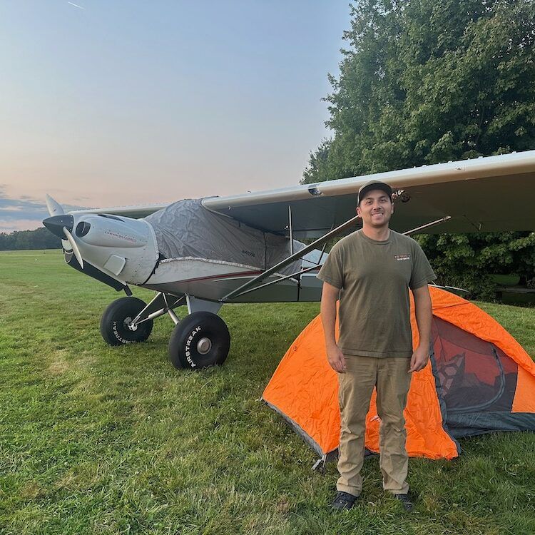A man is standing next to an orange tent in front of an airplane