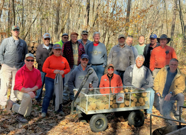 A group of people are posing for a picture with a wagon full of logs.