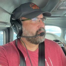 A man wearing a hat and headphones is sitting in a plane.