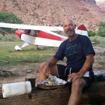 A man is sitting on a log in front of an airplane