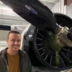 A man stands in front of an airplane with the propeller open