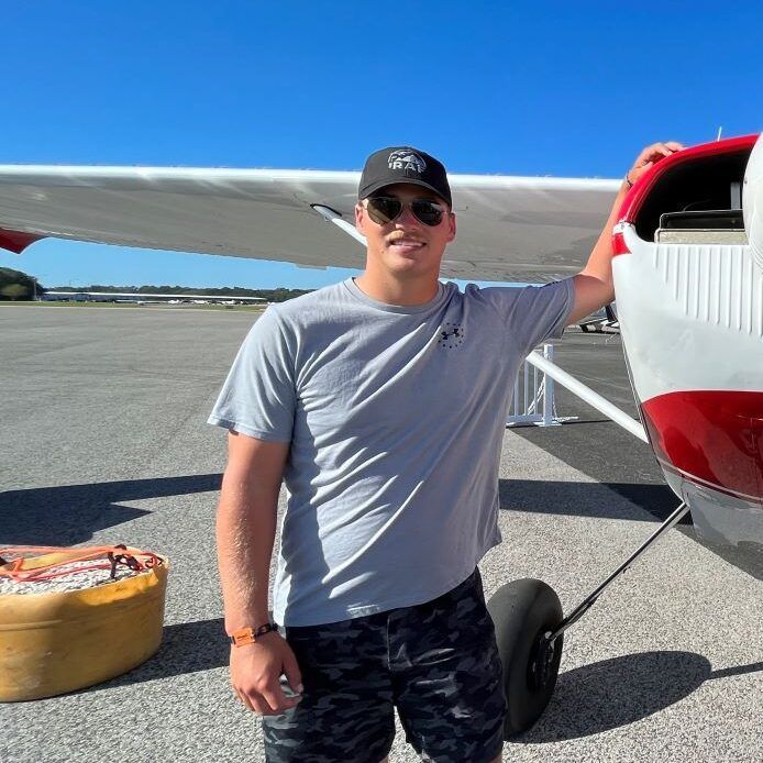 A man wearing sunglasses and a hat is standing in front of an airplane