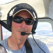 A man wearing headphones and sunglasses is sitting in a plane.