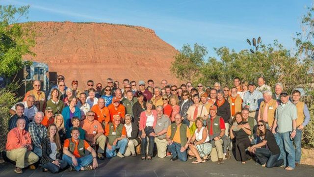 A large group of people are posing for a picture in front of a mountain.