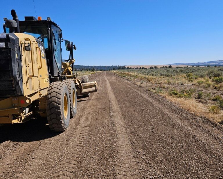 A yellow tractor is driving down a dirt road