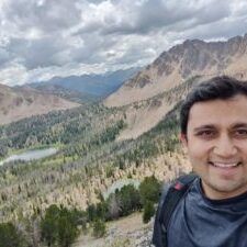 A man is taking a selfie in front of a mountain range.