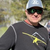 A man wearing a hat and sunglasses is standing in a field.