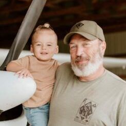 A man is holding a baby in front of an airplane.
