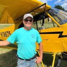 A man is standing in front of a yellow airplane.