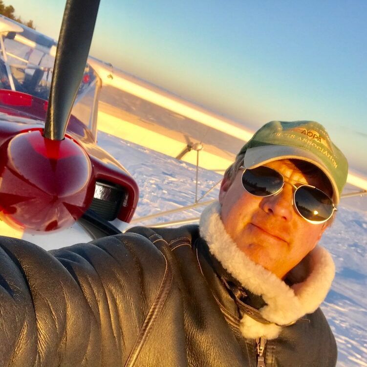 A man wearing sunglasses is taking a selfie in front of an airplane