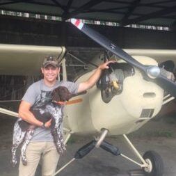 A man is holding a dog in front of a small plane.