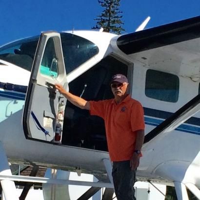 A man in an orange shirt is standing in front of an airplane