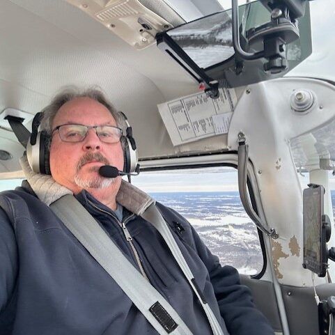 A man wearing headphones and a seat belt is sitting in the cockpit of an airplane.