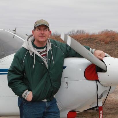 A man in a green jacket leans against a small plane