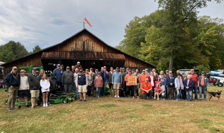 A large group of people are standing in front of a barn.