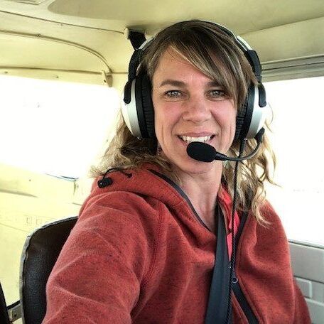 A woman wearing headphones and a microphone is sitting in a plane.
