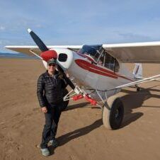 A man is standing next to a small plane on a dirt field.