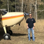 A man is standing in front of a small plane in a field.