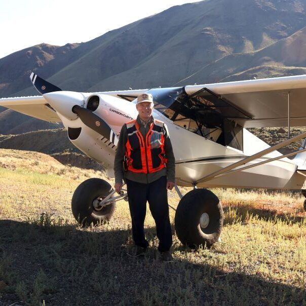 A man in an orange vest stands in front of a small plane