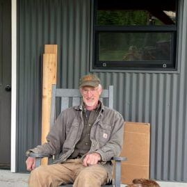A man is sitting in a chair on a porch next to a dog.