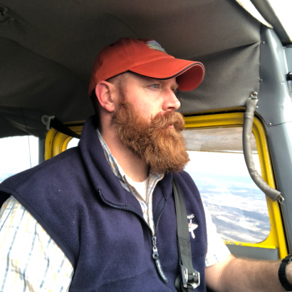 A man with a beard wearing an orange hat and a blue vest