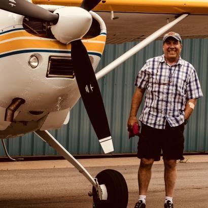 A man in a plaid shirt is standing in front of an airplane