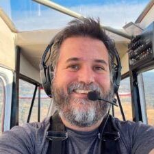 A man with a beard and headphones is taking a selfie in a plane.