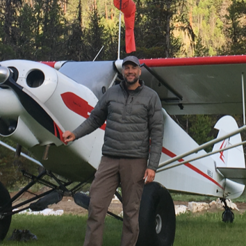 A man stands in front of a small plane with a red tail