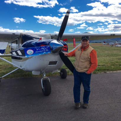 A man stands in front of a small plane with a blue banner on the side that says ' rescue to life '