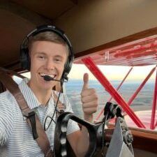 A man wearing headphones is giving a thumbs up while sitting in the cockpit of an airplane.